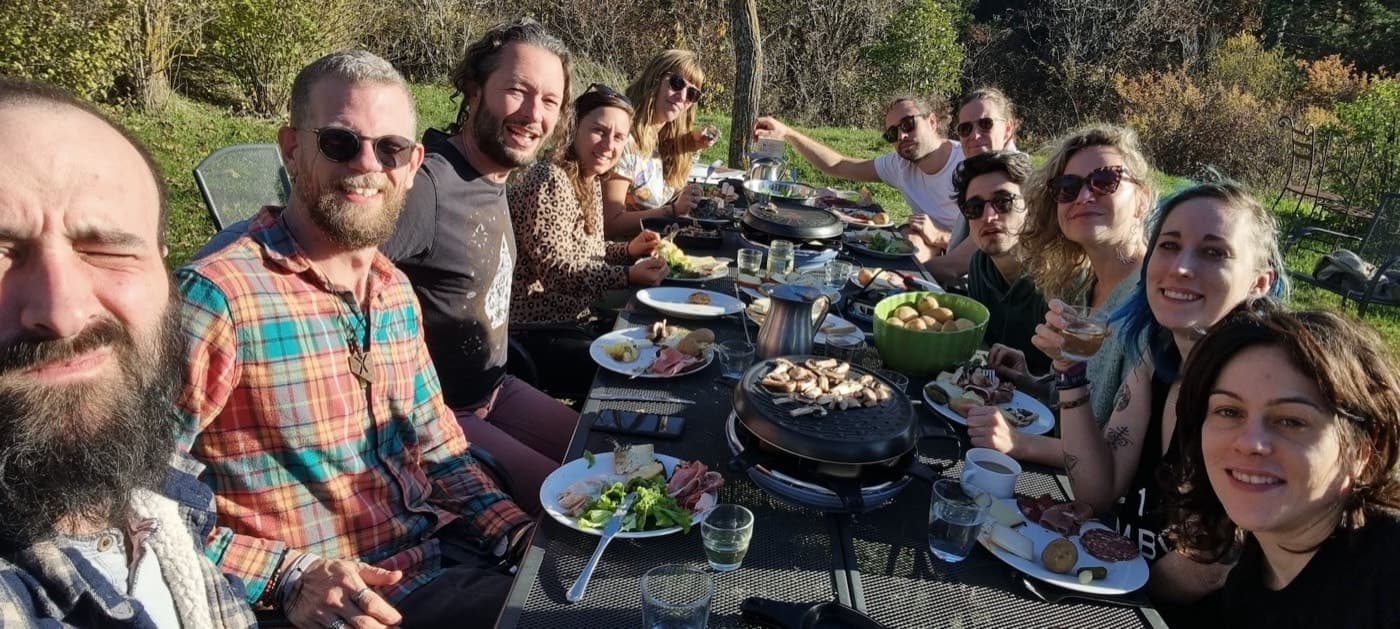 La tablée d'un coliving en plein soleil : une dizaine d'amis rient autour des restes du déjeuner